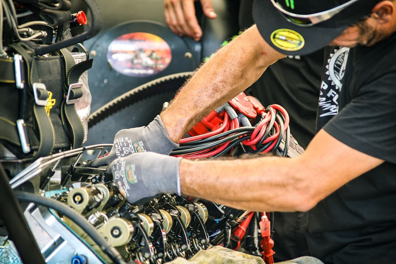 Gloved hands working under a car bonnet